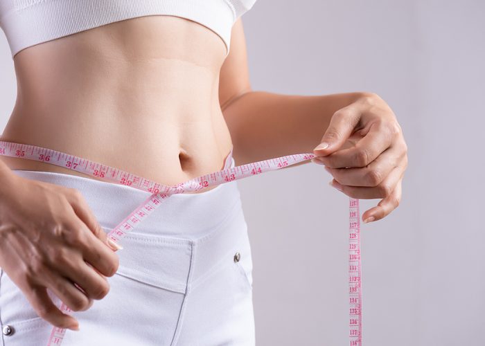Close up slim young woman measuring her thin waist with a tape measure. Healthcare and woman diet lifestyle concept to reduce belly and shape up healthy stomach muscle.